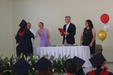 Una de las graduadas recibe su diploma de manos de Jole Segers, gerente de Bakery School Puratos, durante la ceremonia de graduación de la primera promoción de Bakery School El Salvador. En la mesa de honor estuvieron presentes el P. Guillermo Argüello, director de la Obra Salesiana San José; Rafael Servián, representante legal de Bakery School El Salvador; e Ing. Andrea López, directora de la institución.