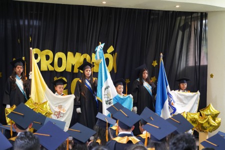 Los abanderados del Centro Escolar Miguel Magone portan con orgullo las banderas de Guatemala, la Iglesia y la institución durante la ceremonia de clausura del año escolar.