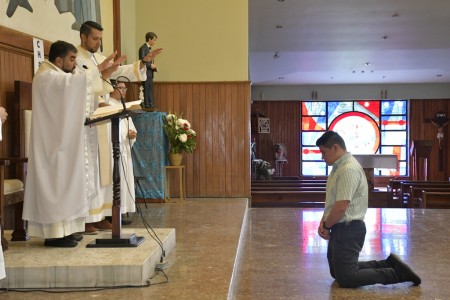 El hermano Daniel Núñez, de rodillas, recibe la bendición del padre Julio Navarro, SDB, durante la misa de envío misionero en el Templo Santo Domingo Savio del Instituto Técnico Ricaldone.