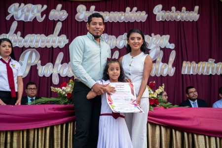 Estudiante festeja su promoción junto a sus padres, en un ambiente de alegría y orgullo.