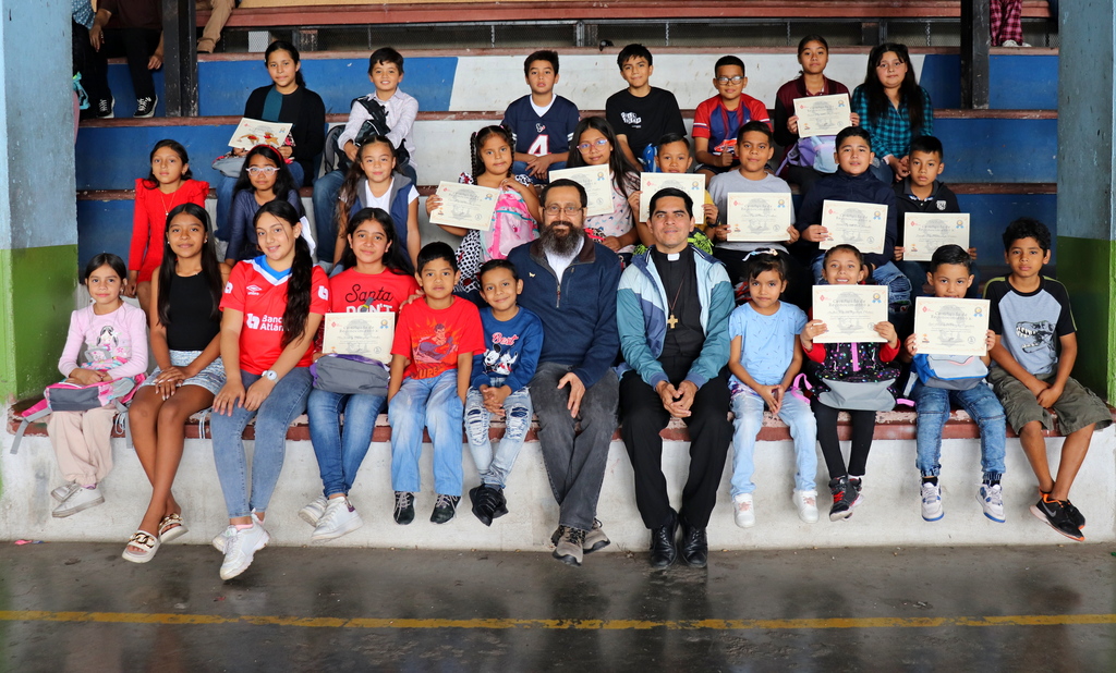  Niños becados posan al finalizar el acto de clausura, celebrando sus logros académicos junto a miembros de la comunidad parroquial.