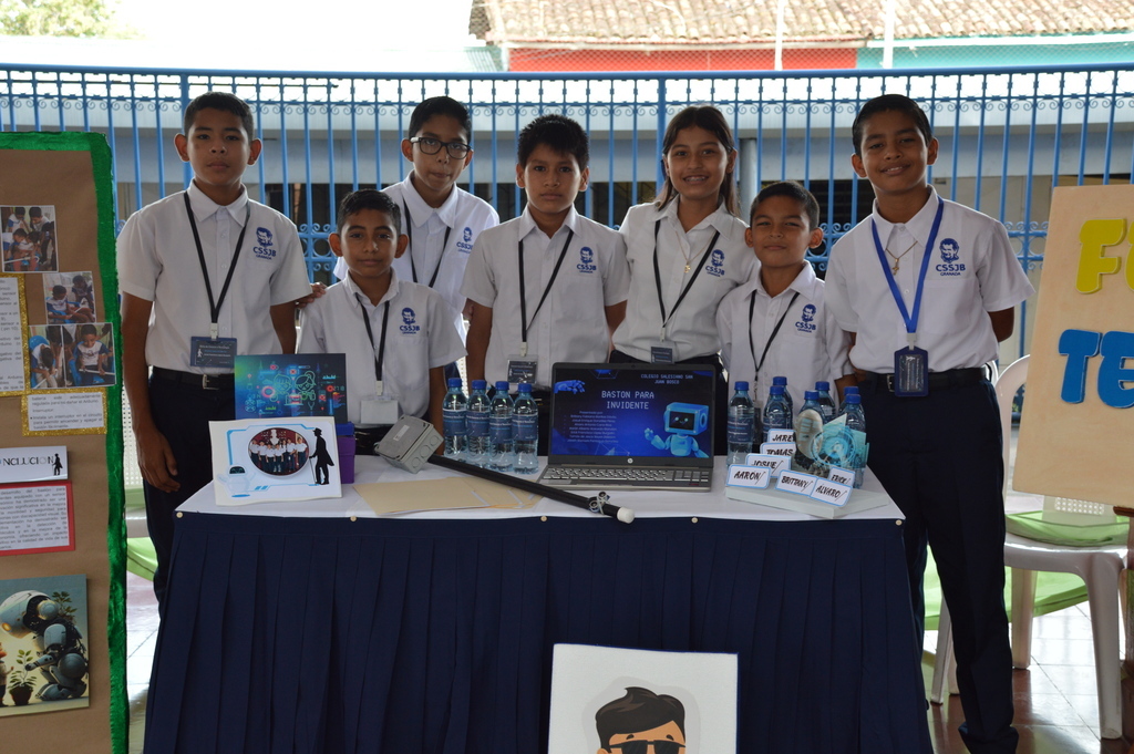 Estudiantes del Colegio Salesiano San Juan Bosco presentan orgullosamente su proyecto de bastón inteligente para invidentes en la Feria de Tecnología. 