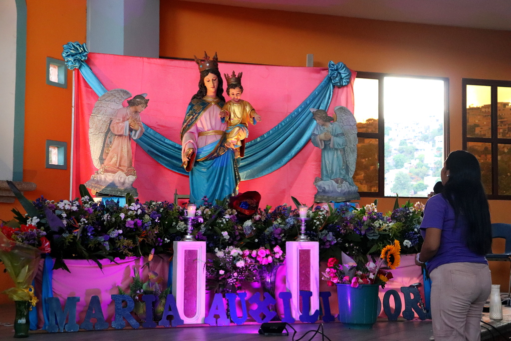 Una joven reza el Santo Rosario con devoción frente al altar adornado de María Auxiliadora, expresión viva de fe y amor filial a la Madre de los jóvenes.